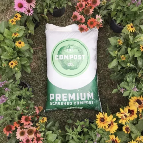 The Compost Company's organic bagged compost placed on a flower bed in full bloom.